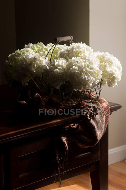 Fresh cut hydrangea flowers in wire basket on wooden small cabinet — Stock Photo