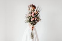Наречена в білій весільній сукні, що тримає букет квітів, білий фон — стокове фото