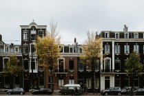 Scenic cityscape of Amsterdam street with cars, people bicycles by typical houses facades — Stock Photo