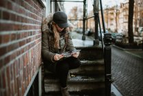 Frau sitzt auf der Treppe vor der Straße und schaut auf die Karte — Stockfoto