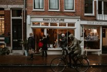 Típica calle Amsterdam con gente que pasa por la tienda de la alta costura de la lluvia en tiempo lluvioso - foto de stock
