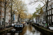 Famosa vista del paisaje urbano de Ámsterdam con arquitectura tradicional, bicicletas, puente sobre el canal y barcos amarrados - foto de stock