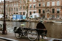 Visão traseira do jovem sentado no banco com bicicleta olhando para o canal de Amsterdam — Fotografia de Stock