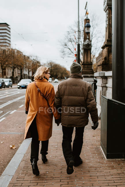 Vue arrière du couple marchant par la rue de la ville tenant la main — Photo de stock