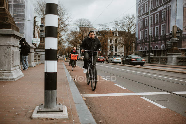 Man and woman riding bicycles by the road, urban cityscape on background — Stock Photo