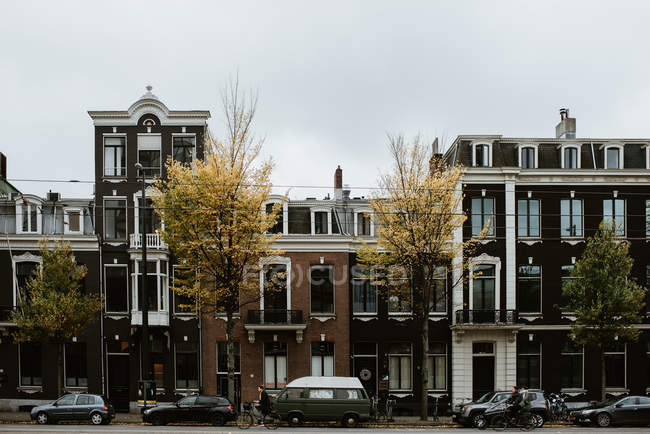 Paisagem cityscape cênica de Amsterdam rua com carros, pessoas bicicletas por casas típicas fachadas — Fotografia de Stock