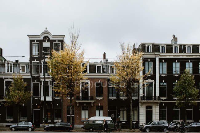 Paisagem cityscape cênica de Amsterdam rua com carros, pessoas bicicletas por casas típicas fachadas — Fotografia de Stock