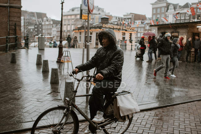 Hombre asiático montando bicicleta en la calle Amsterdam con tiempo lluvioso, Países Bajos - foto de stock