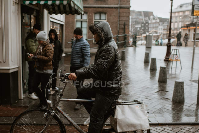 Hombre asiático montando bicicleta en la calle Amsterdam con tiempo lluvioso, Países Bajos - foto de stock