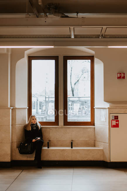 Молодая женщина, сидящая на чудном подоконнике на станции — стоковое фото