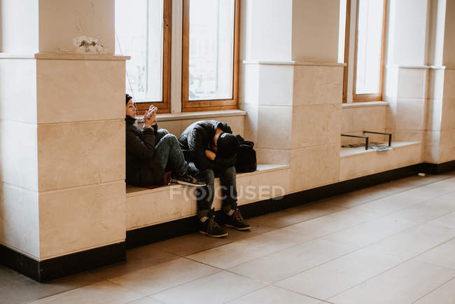 Jovem casal sentado no peitoril da janela na estação, parecendo cansado — Fotografia de Stock