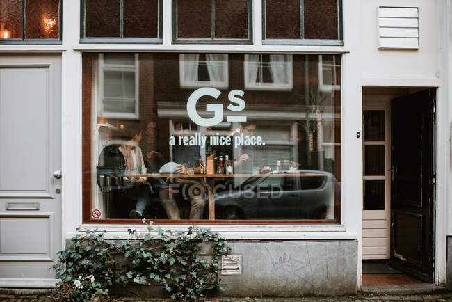 Vista exterior do café de rua com pessoas sentadas dentro do painel de vidro da janela, Amsterdã, Países Baixos — Fotografia de Stock