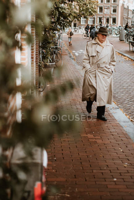 Пенсионер в плаще и шляпе, идущий по улице в старом городе Амстердама, Нидерланды — стоковое фото