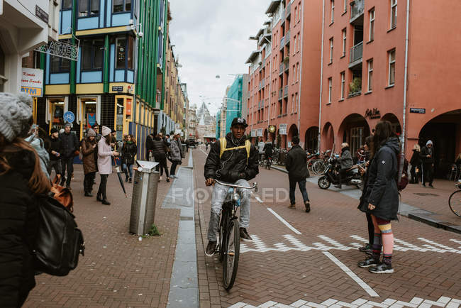Joven montando en bicicleta en la calle llena de gente, Amsterdam, Países Bajos - foto de stock