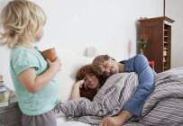 A couple lying in bed with their child standing beside the bed — Stock Photo