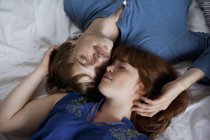 Una joven pareja acostada cabeza a cabeza en una cama, con los ojos cerrados - foto de stock