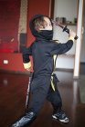 A boy dressed in a ninja costume swinging a samurai sword — Stock Photo