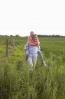 A man giving his girlfriend a piggy back ride through a field — Stock Photo