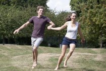 Young couple holding hands and running in park — Stock Photo