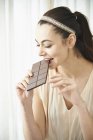 Happy woman eating large chocolate bar at home — Stock Photo