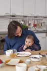 Father looking at baby girl eating bread at home — Stock Photo