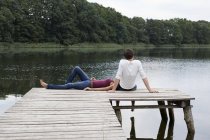 Pareja joven relajándose en el muelle de madera en el lago en la naturaleza - foto de stock