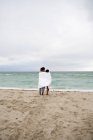 Молодая пара, завернутая в пляжное полотенце, стоящее на пляже — стоковое фото