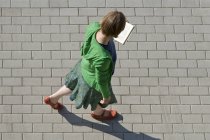 Сверху женщина ходит по улице и читает книгу — стоковое фото