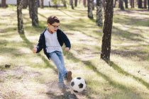 Niño feliz jugando fútbol en el bosque - foto de stock