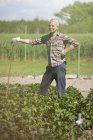 Улыбающийся взрослый мужчина с палкой, стоящий в огороде — стоковое фото