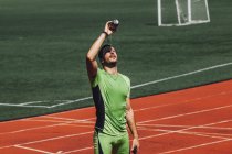 Joven atleta masculino vertiendo agua en la cara en el estadio - foto de stock