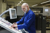 Mature man doing quality check of printout with scanner at printing press — Stock Photo