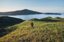 Rear view of hiker standing on grassy field and looking at sea — Stock Photo