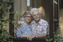 Portrait of Thoughtful smiling senior couple standing at window — Stock Photo
