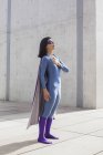 Уверенная женщина в костюме супергероя, стоящая на полу за стеной — стоковое фото
