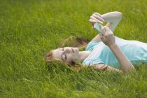 Mujer joven usando el teléfono mientras está acostado en el campo cubierto de hierba - foto de stock