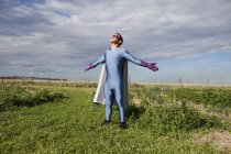 Homem em traje de super-herói de pé com os braços estendidos no campo gramado — Fotografia de Stock
