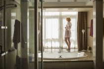 Mulher loira em pé na janela no banheiro moderno — Fotografia de Stock