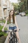 Mujer sonriente en bicicleta en la calle empedrada contra edificios en la ciudad - foto de stock
