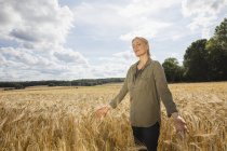 Mujer pensativa de pie en medio de la cosecha de trigo en la granja - foto de stock