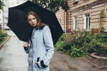 Retrato de adolescente sosteniendo paraguas de pie en la calle de la ciudad - foto de stock