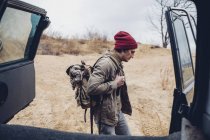 Uomo che trasporta lo zaino mentre cammina nella foresta visto attraverso il bagagliaio del veicolo aperto — Foto stock