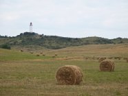 Lighthouse overlooking hay bales on sunlit grassland — Stock Photo