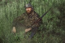 Hunter holding rifle while sitting on grassy field — Stock Photo