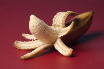Plátano pelado sobre fondo rojo - foto de stock