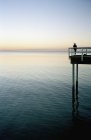 Silhouette of person fishing at end of pier at scenic seascape — Stock Photo