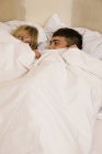 Jovem casal na cama com edredom puxado até os olhos — Fotografia de Stock