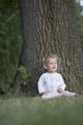 A baby girl sitting under a tree and looking away — Stock Photo