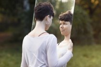 Vista trasera de la mujer sosteniendo el espejo y mirando el reflejo en el parque - foto de stock