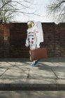 Astronauta caminando por la acera de la ciudad y llevando maleta - foto de stock